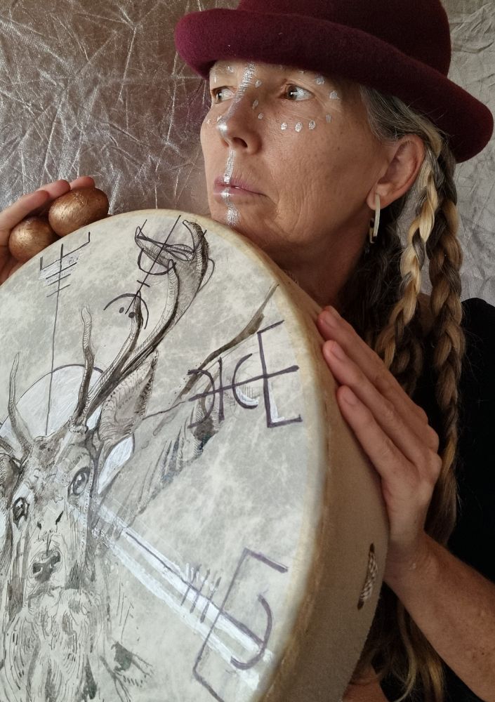 Woman with painted face holding a painted shaman drum looking up